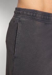 Σκούρο γκρι αθλητικά σορτς με υφασμάτινη ζώνη και τσέπη στο πλάι. Το ύφασμα φαίνεται απαλό και ελαστικό, σχεδιασμένο για άνεση και κινητικότητα.