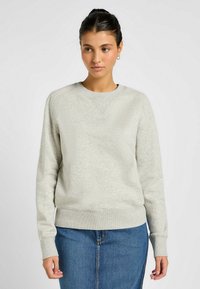 Sudadera gris claro con cuello redondo, tejido texturizado y puños acanalados. Combinada con una falda de mezclilla, que presenta una cintura ajustada.