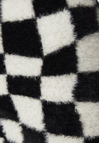 Tissu à carreaux noir et blanc avec une texture fuzzy, présentant des carrés alternés de tailles variées dans un design en tricot doux.