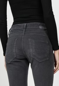 Graue Corduroy-Jeans mit enganliegendem Design, ausgestattet mit zwei Gesäßtaschen und subtilen Stichdetails. Der Stoff hat eine strukturiertes Aussehen.