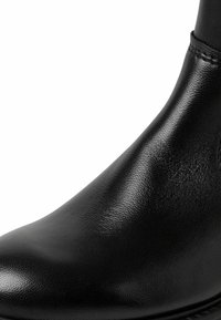 Botín negro de cuero hasta el tobillo con una textura suave y un diseño aerodinámico, que presenta un ligero brillo y acentos de costura mínimos.