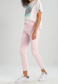 Rosa denimjeans med en avskuren nederkant, i kombination med en lös vit t-shirt med grafiskt tryck och vita sneakers. Slät textur, avslappnad passform.