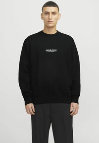 Sweatshirt noir avec un col rond, des poignets et un ourlet côtelés. Présente le branding blanc "Jack & Jones" sur la poitrine. Tissu doux et texturé.