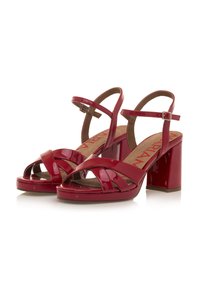Sandalias de tacón alto de charol rojo con tiras entrecruzadas, puntera abierta y tacones de bloque. Incluye una correa de tobillo ajustable.