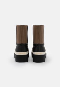 Černé gumové kotníkové boty s hnědými prošívanými textilními svršky, krémovými akcenty a robustní černou podrážkou. Branding viditelný na podpatku.