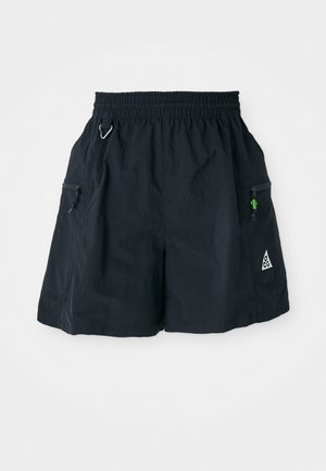 Svarte shorts laget av lettvevde materialer, med elastisk midje, sidelommer med glidelås, og en trekantet logo på kanten.