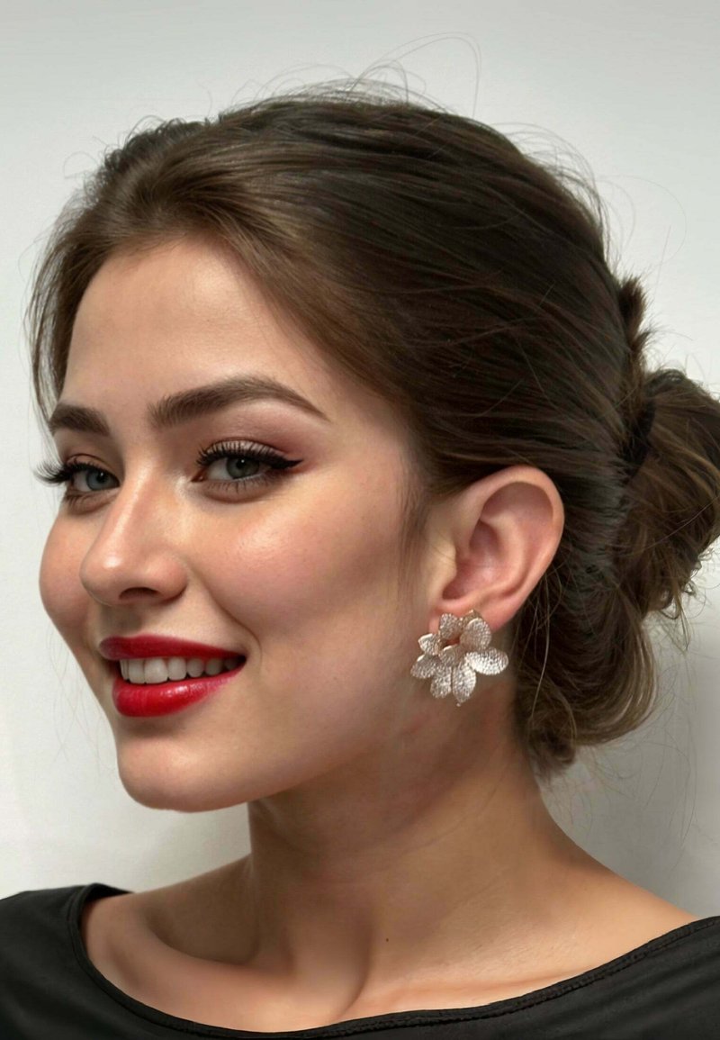Silver floral earrings with textured petals and a rose gold accent, worn by a person with medium-length hair and red lipstick.