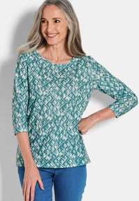 Türkis gemusterte Bluse mit rundem Ausschnitt und 3/4-�Ärmeln. Besitzt ein geometrisches Design in helleren Farbtönen. Hergestellt aus weichem Stoff.