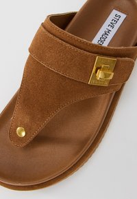 Brown suede and leather sandal with gold buckle and rivet details, featuring the Steve Madden brand label on the insole.