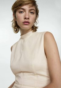 Helles beige, ärmelloses Kleid mit hohem Ausschnitt, aus einem glatten, leicht strukturierten Stoff gefertigt. Verfügt über dezente Nähte und eine figurbetonte Silhouette.