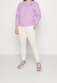 Felpa lilla chiaro con polsini a coste, pantaloni della tuta bianchi e scarpe da ginnastica rosa chiaro. Design semplice, vestibilità casual, senza motivi visibili.