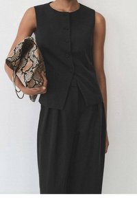 Černý bezrukávový top s pěti knoflíky a přiléhavým střihem, doplněný volnými černými kalhotami a vzorovanou béžovou a černou kabelkou.