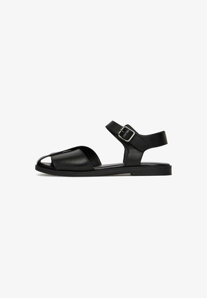 Sandali in pelle nera con design a punta aperta, cinturino alla caviglia con fibbia e suola piatta per il massimo comfort.