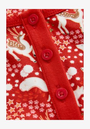 Közelkép piros anyagról piros gombokkal, amelyen fehér medvék, rénszarvasok, narancssárga csillagok és virágok találhatóak ünnepi mintában.