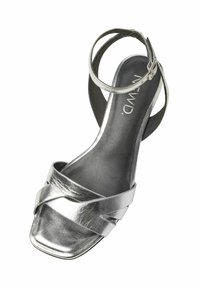 Silver metallisk remsand med fyrkantig tå, som har överkorsade remmar och en vristrem. Slät textur och låg klackdesign.