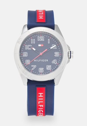Marineblaue Silikon-Uhr mit rundem silbernen Gehäuse, weißem Ziffernblatt, roten Akzenten und "HILFIGER"-Logo. Verfügt über eine drehbare Lünette und eine Edelstahlkrone.