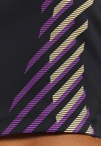 Tejido atlético negro con rayas diagonales en púrpura y amarillo. La textura es suave con un ligero brillo en la superficie.