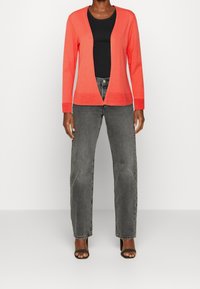 Korallfärgad cardigan, öppen framsida, lång ärm, ribbad nederkant, ihop med en svart tanktopp och grå vida jeans. Mjuk, lätt textur.