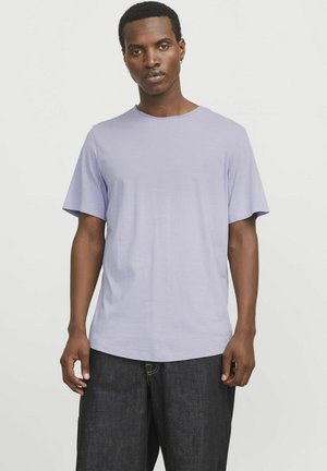 Camiseta de cuello redondo en color lavanda, hecha de una tela suave, con manga corta; presenta un corte holgado y una textura suave, combinada con unos jeans oscuros.