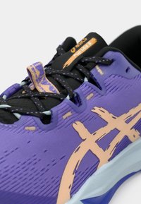 Lilla sportsko med en tekstureret overdel, der har et beige logomønster, sorte snørebånd og en lys blå sål. Inkluderer en trækstrop.