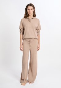 Beige hoodie met trekkoord, ribgebreide manchetten, gecombineerd met bijpassende wijde broek van een zachte breimateriaal. Geen patronen of accenten.
