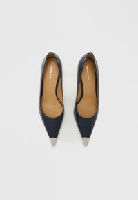 Mørkeblå lærhøye hæler med spisse tær og metalliske sølvspisser. Glatt tekstur, mandelformede utskjæringer og beige innersåler.