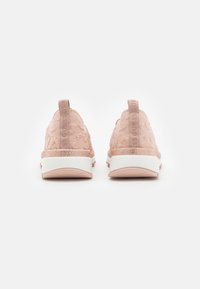 Une paire de baskets à enfiler rose clair avec un tissu en maille texturé, des poignées de traction et des semelles blanches, vues de l'arrière sur fond blanc.