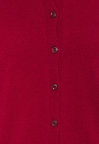 Cardigan rosso lavorato a maglia con scollo rotondo e sei bottoni scuri sul davanti. La texture è liscia e uniforme.