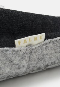 Grå toffla med svart ullfoder, sömmar runt kanterna och en liten etikett med "FALKE" i guldskrift. Mjuk textur.
