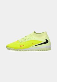 Zapato de fútbol Nike de color amarillo neón con logotipos de swoosh en negro y rojo, cuello tipo calcetín en el tobillo y suela texturizada para uso en césped.