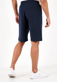 Pantaloni sportivi blu navy con vita elastica e tasche laterali, caratterizzati da una texture liscia e un design lungo fino al ginocchio.
