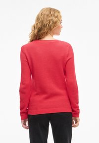 Punainen neulottu neulepaita, jossa on teksturoitu pinta, resorit hihansuissa ja helmassa, pitkät hihat ja pyöreä kaula-aukko.