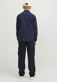 Granatowa koszula z długim rękawem o prostym kroju, zestawiona z granatowymi spodniami typu cargo z bocznymi kieszeniami oraz białymi trampkami. Prosty design, gładka tkanina.