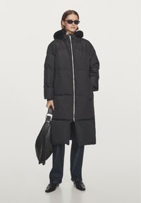 Gevoerd zwart coat met een nepbontkraag, ritsluiting, zijzakken en een split. Draagt bij donkere denim en zwarte leren accessoires.