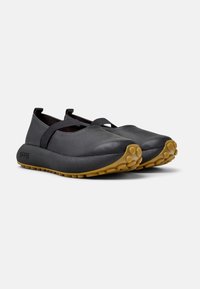 Black leather shoes with an elastic strap across the forefoot, rounded toe, and a gum rubber sole featuring textured grip patterns.