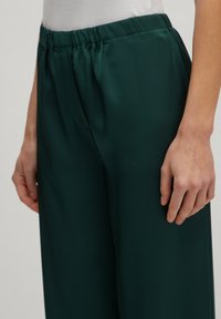 Groene, lichte broek met een elastische tailleband en een rechte snit. Glad textuur zonder zichtbare patronen of hardware-details.