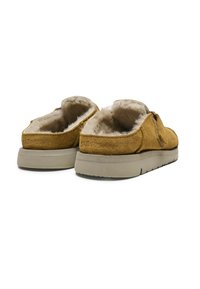 Zapatos de ante marrón sin cordones con un suave forro de piel, suela plana y un sutil logotipo grabado en el talón. Con un diseño casual y un respaldo redondeado.