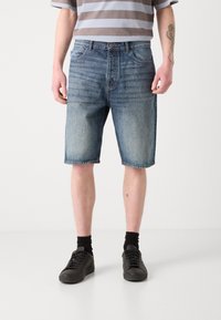 Denim-shorts med en lys blå til mørk blå gradient, fem-lomme design, rett snitt og synlige sømmer. Kombinert med svarte sneakers.