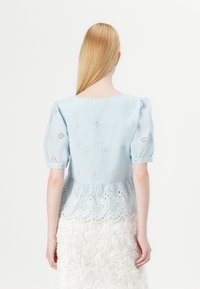 Blusa azzurro chiaro a maniche corte con motivi floreali ricamati, orlo peplo e scollatura arrotondata. Vista posteriore, tessuto morbido.