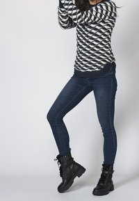 Námořnický a bílý vzorovaný pletený svetr v kombinaci s tmavými džíny a černými šněrovacími kotníkovými botami s robustní podrážkou a kožešinovým podšívkou.