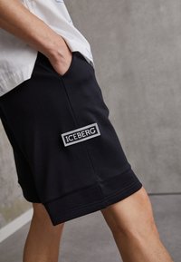 Czarne, krótkie spodenki o średniej długości, wykonane z miękkiego materiału. Posiadają białą naszywkę z logo Iceberg z boku. Prosty design z prostym krojem.