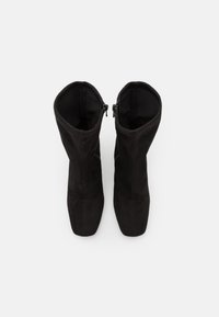 Bottes noires mi-mollet à bouts carrés, coutures visibles et fermetures éclair sur les côtés intérieurs, vues d'en haut sur fond blanc.