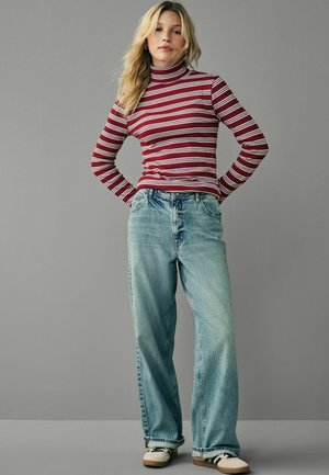 Gestreepte rood-witte coltrui, hooggewaisted lichtblauwe jeans, relaxte pasvorm, gecombineerd met sneakers. Tegen een neutrale achtergrond.