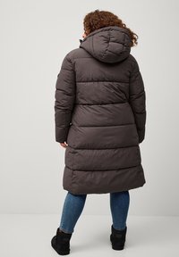 Cappotto imbottito lungo di un grigio scuro con cappuccio, caratterizzato da sezioni cucite orizzontalmente, una chiusura con zip e tasche laterali.