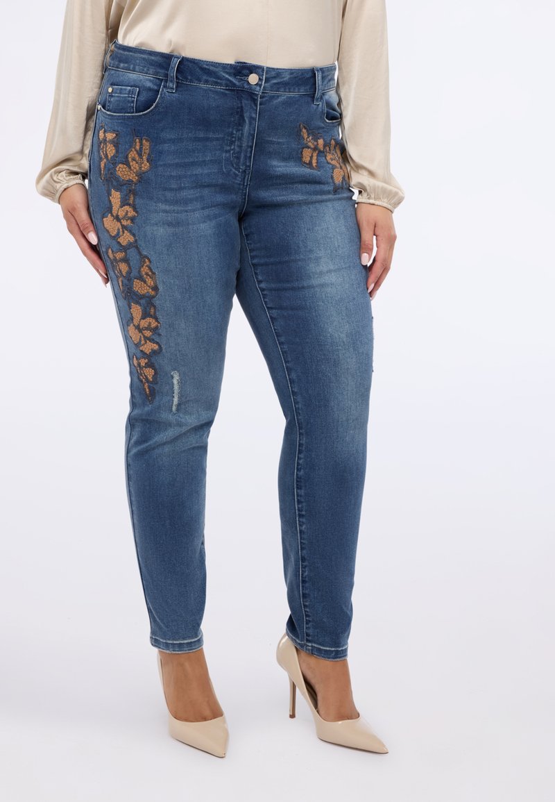Ciemnoniebieskie jeansy z denimu z kwiatowym haftem w metalicznym odcieniu brązu, dopasowany krój i lekko przetarte detale na prawej udzie.