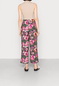 Květinové kalhoty širokého střihu v černé barvě s růžovými a hnědými vzory, doplněné béžovým žebrovaným tílkem a černými sandály. S volným střihem.