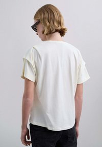 Camiseta blanca de algodón con mangas cortas, cuello redondo y corte relajado. Textura suave con una silueta ligeramente holgada.