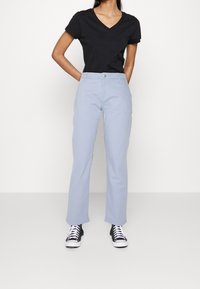 Jasnoniebieskie spodnie o prostych nogawkach, z kieszeniami po bokach i metalowym zapięciem. W zestawie z czarnym t-shirtem w serek i czarnymi trampkami.