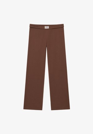 Brązowe spodnie z szerokimi nogawkami, z podwiniętym pasem i małą białą metką z logo umieszczoną centralnie z przodu.