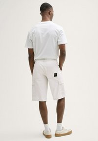 Vita cargoshorts med två sidofickor, bakficka och en liten svart etikett. Kombinerat med en vit t-shirt och beige sneakers.